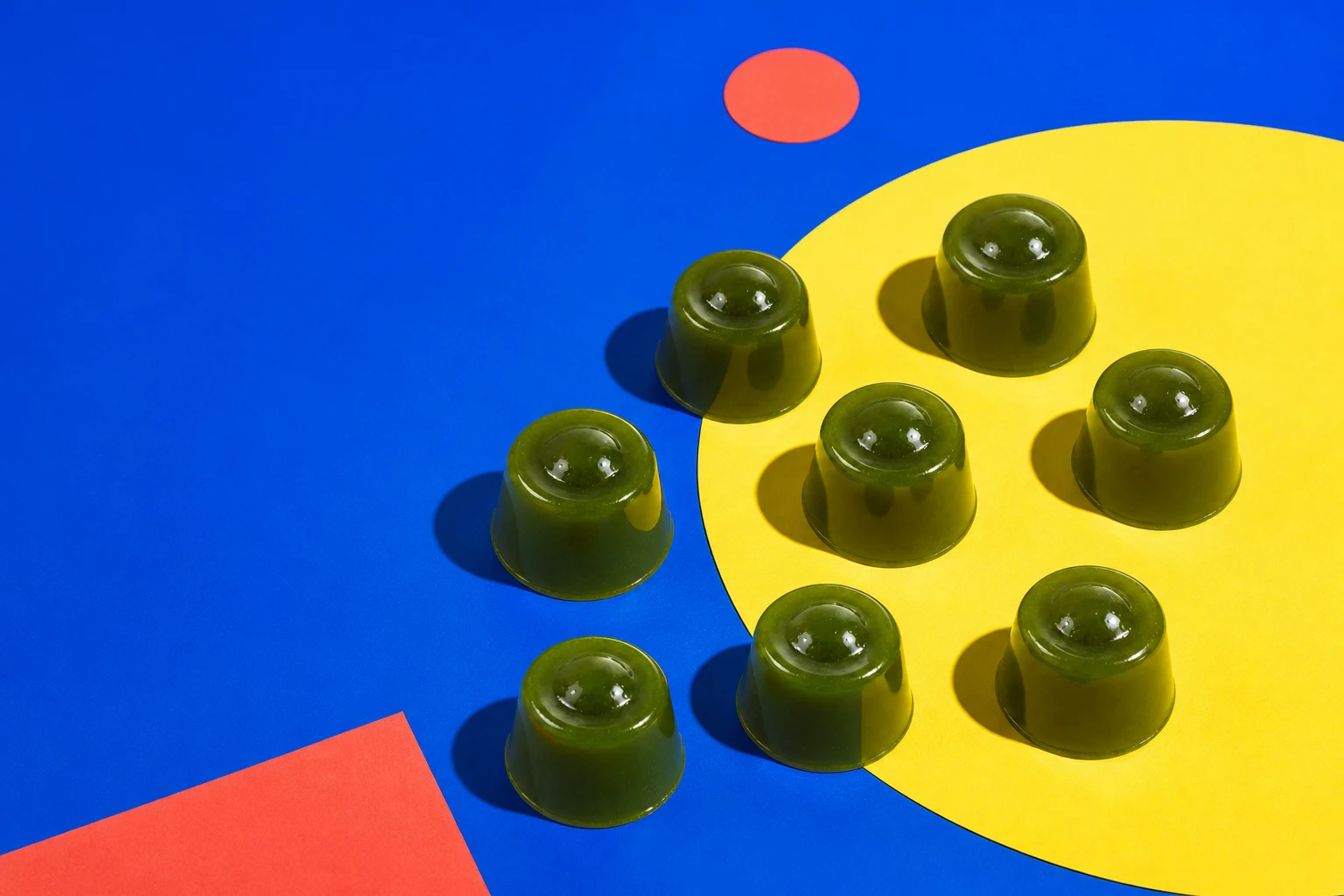 Glossy matcha jellies on bright cobalt and yellow paper
